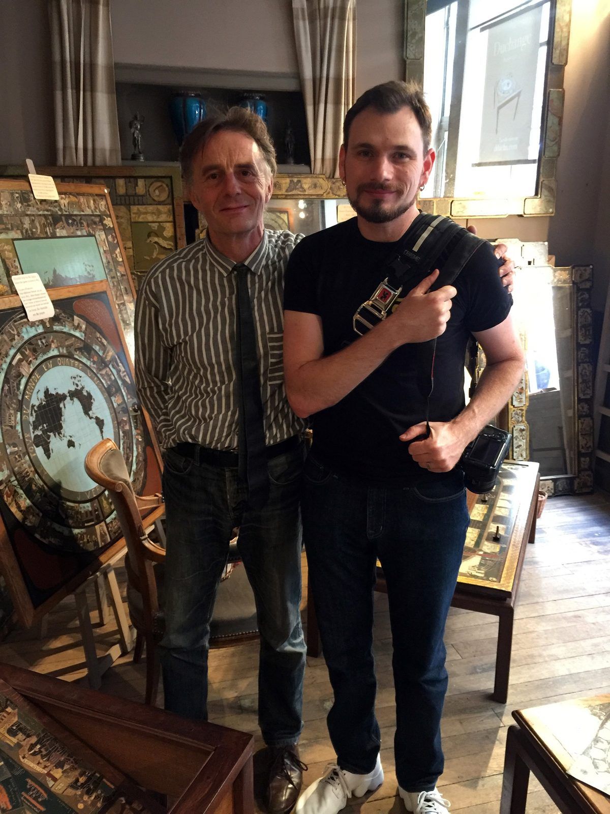 Colin standing with Dominique Duchange, a lean man in a striped shirt and dark tie, in his shop among lacquered board games and gilt mirrors.