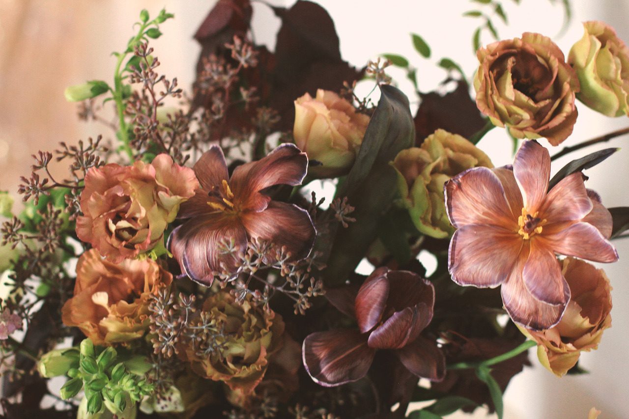Close-up of the bridal bouquet: copper lisianthus, plum tulips, seeded eucalyptus and green sprigs against a soft peach background.