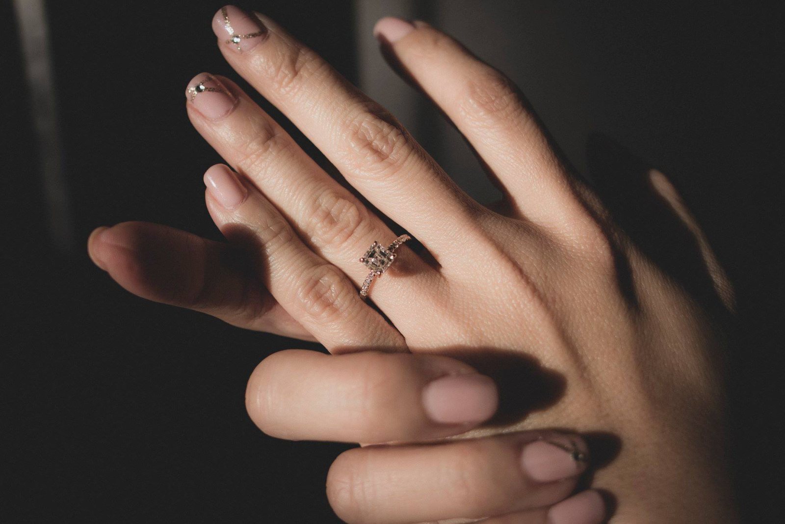 A hand wearing the ring, resting against a second hand in low light against a dark background.